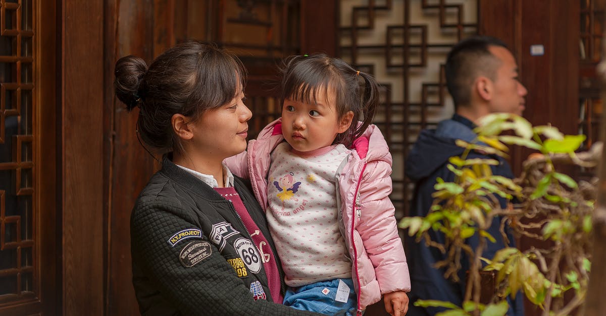 Same Global Entry membership/PASSID number for husband and wife? - Smiling ethnic mom embracing charming toddler child against father and ornamental building wall in daylight