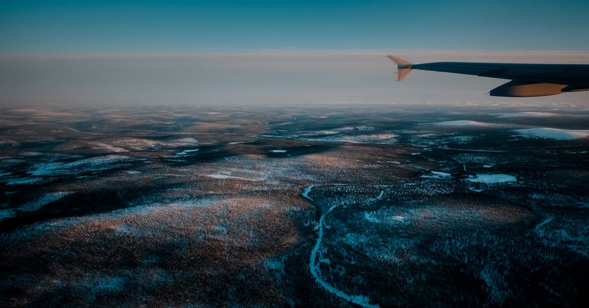 Schengen: connecting flight at the destination country - View from airplane of wild snowy valley with curvy frozen rivers located in vast deserted terrain in winter evening Schengen: connecting flight at the destination country - View from airplane of wild snowy valley with curvy frozen rivers located in vast deserted terrain in winter evening