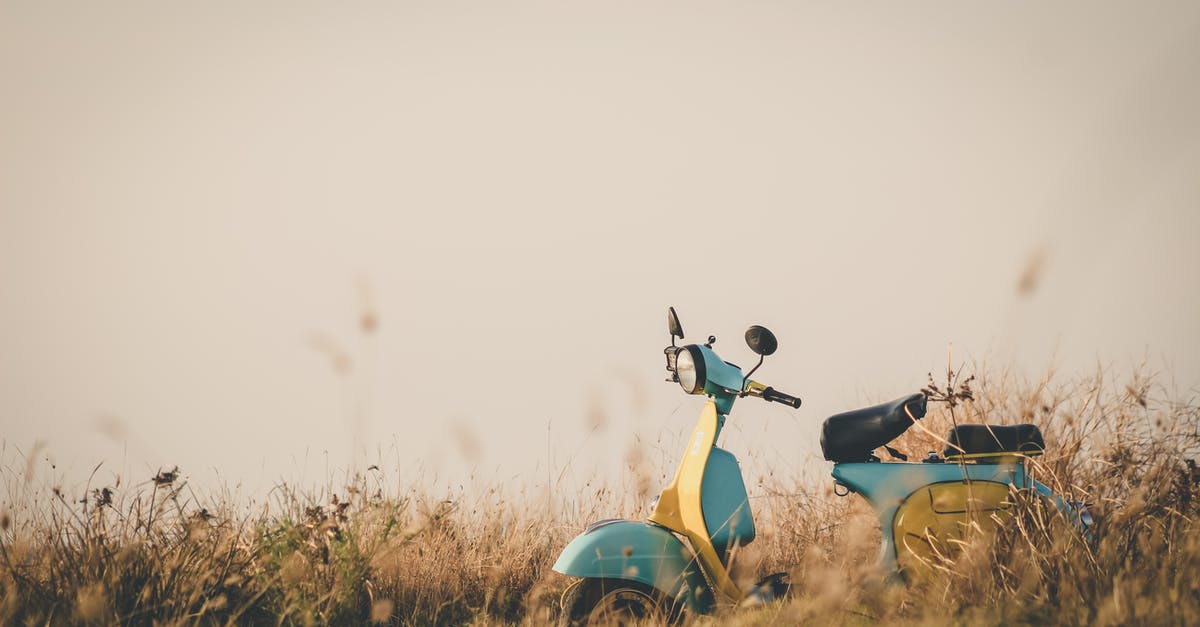 Schengen Tourism Visa Field 20 "Residence in a country other than the country of current nationality" - Vintage blue and yellow motorcycle parked on lawn amidst flowers and grass in countryside on clear day