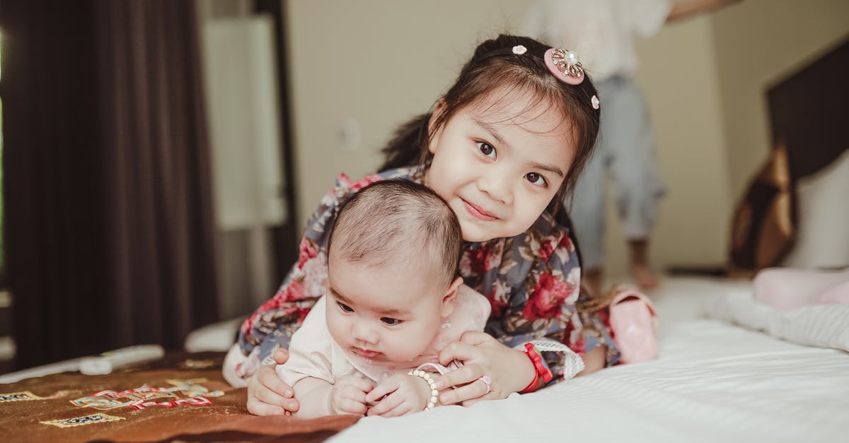 Schengen visa for a US born Baby - Happy Asian girl child embracing newborn baby lying on bed Schengen visa for a US born Baby - Happy Asian girl child embracing newborn baby lying on bed
