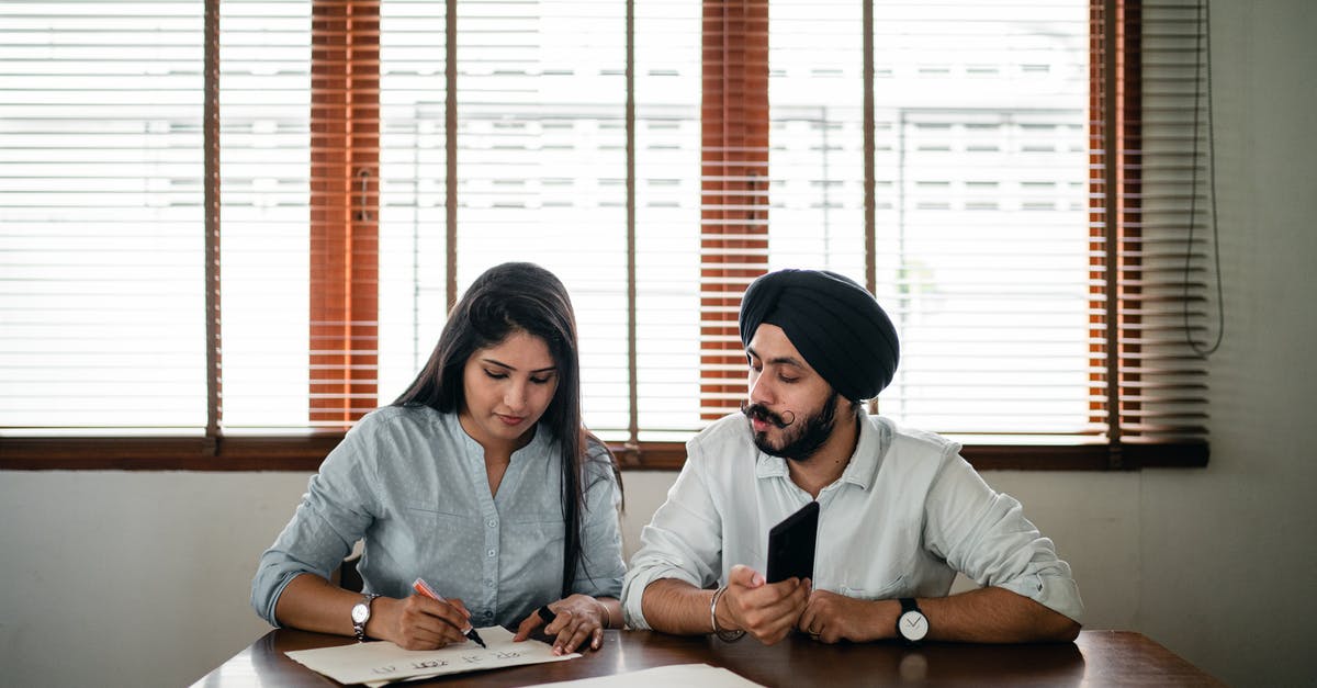 Schengen visa for an Indian student in Ireland - Indian woman with papers and pen writing on paper poster with ethnic Indian man in turban sitting nearby at wooden table Schengen visa for an Indian student in Ireland - Indian woman with papers and pen writing on paper poster with ethnic Indian man in turban sitting nearby at wooden table