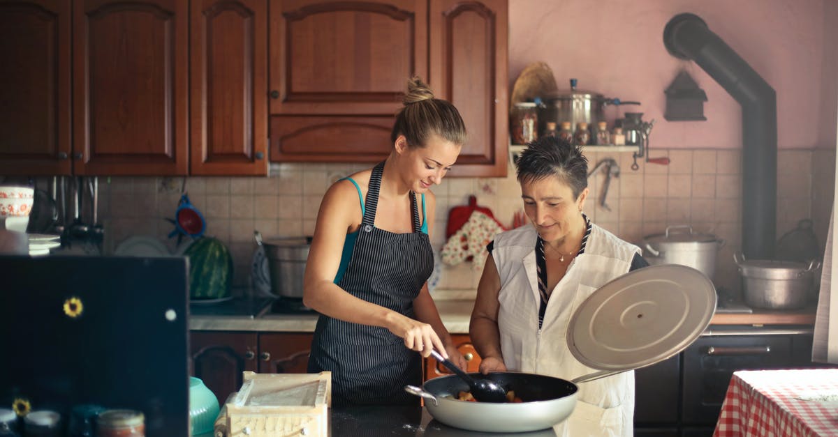 Schengen visa for housewife - Daughter and senior mother standing at table in kitchen and stirring dish in frying pan while preparing food for dinner Schengen visa for housewife - Daughter and senior mother standing at table in kitchen and stirring dish in frying pan while preparing food for dinner