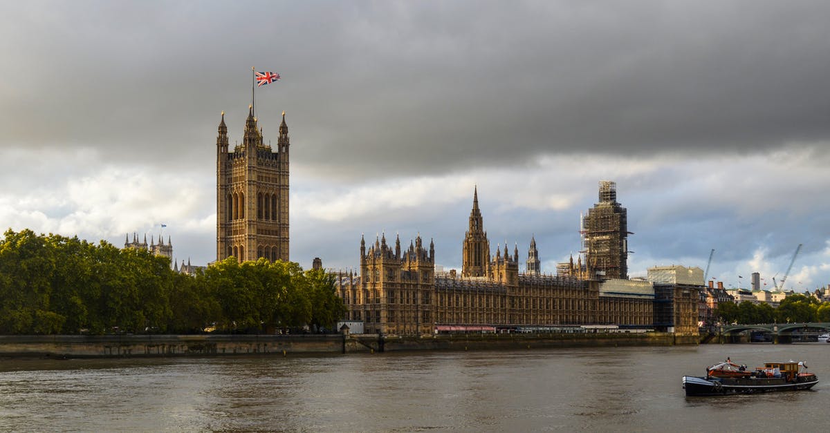 Schengen visa for non-EU child travelling with UK national? - Exterior of Houses of Parliament with flag of England in front of Thames in cloudy day Schengen visa for non-EU child travelling with UK national? - Exterior of Houses of Parliament with flag of England in front of Thames in cloudy day