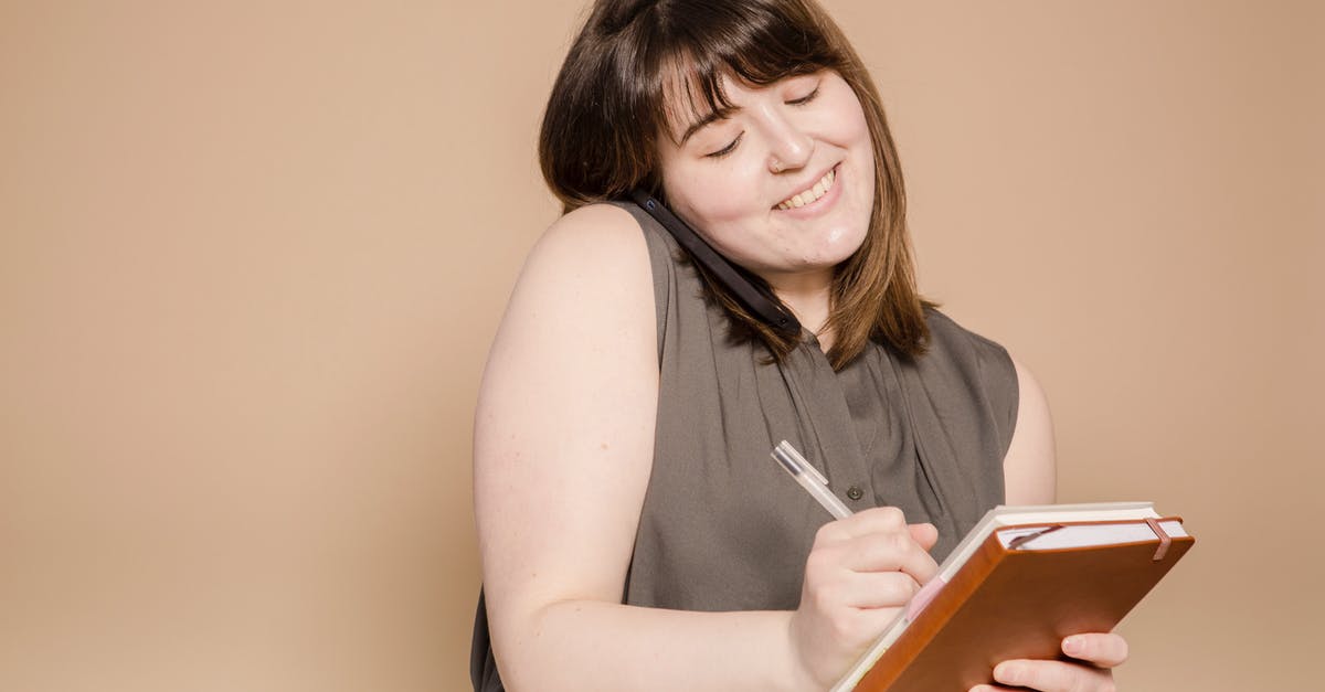 Send 1 overweight suitcase instead of 2 underweight? - Cheerful Asian woman writing in notebook while having phone call Send 1 overweight suitcase instead of 2 underweight? - Cheerful Asian woman writing in notebook while having phone call