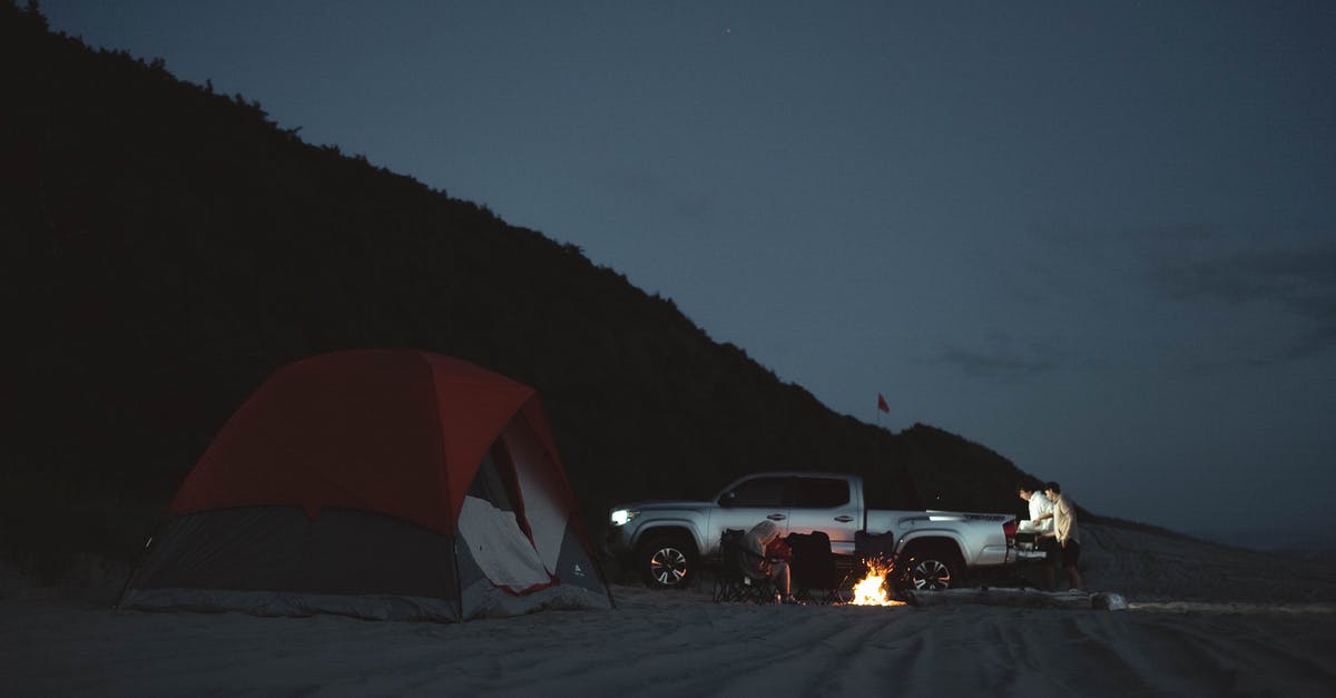 Setting up a tent on a beach in Greece - Anonymous tourists on sandy beach with pick up and burning bonfire near camping tent in night time in nature during campaign Setting up a tent on a beach in Greece - Anonymous tourists on sandy beach with pick up and burning bonfire near camping tent in night time in nature during campaign