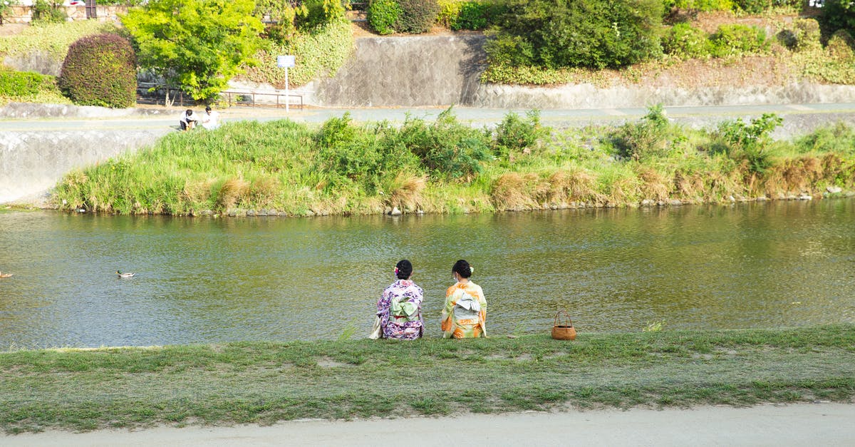 Shore Pass at Narita Airport, Japan - Back view of anonymous ethnic women in traditional kimono apparels contemplating rippled river from coast in town Shore Pass at Narita Airport, Japan - Back view of anonymous ethnic women in traditional kimono apparels contemplating rippled river from coast in town