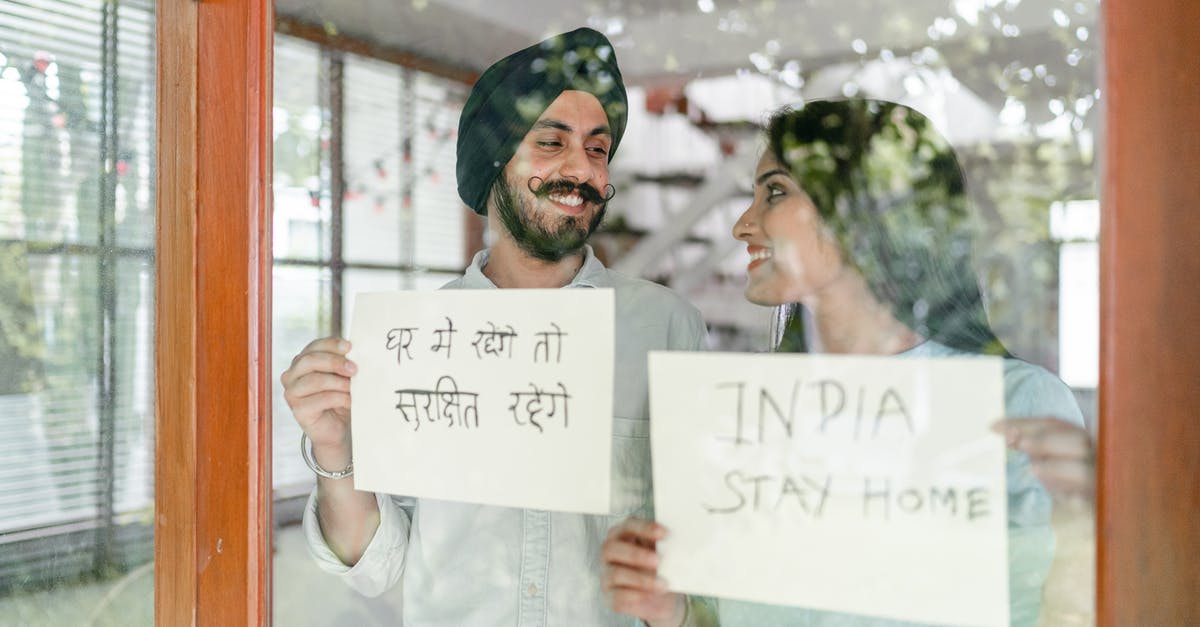 Short Stay Schengen Visa for non Eu spouse - Through glass of young Indian couple standing against window and looking at each other while demonstrating sheets of paper with India stay home inscription in English and Hindi Short Stay Schengen Visa for non Eu spouse - Through glass of young Indian couple standing against window and looking at each other while demonstrating sheets of paper with India stay home inscription in English and Hindi