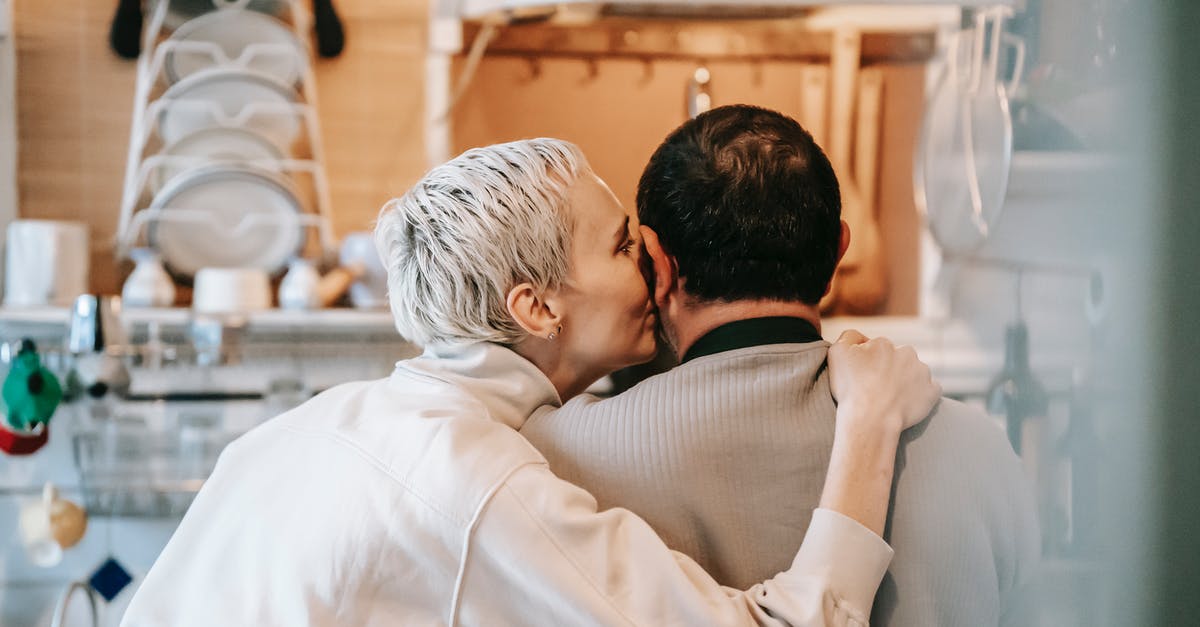 Short Stay Schengen Visa for non Eu spouse - Back view of happy adult woman with short blond hair in casual clothes kissing cheek of anonymous husband while standing together in kitchen Short Stay Schengen Visa for non Eu spouse - Back view of happy adult woman with short blond hair in casual clothes kissing cheek of anonymous husband while standing together in kitchen