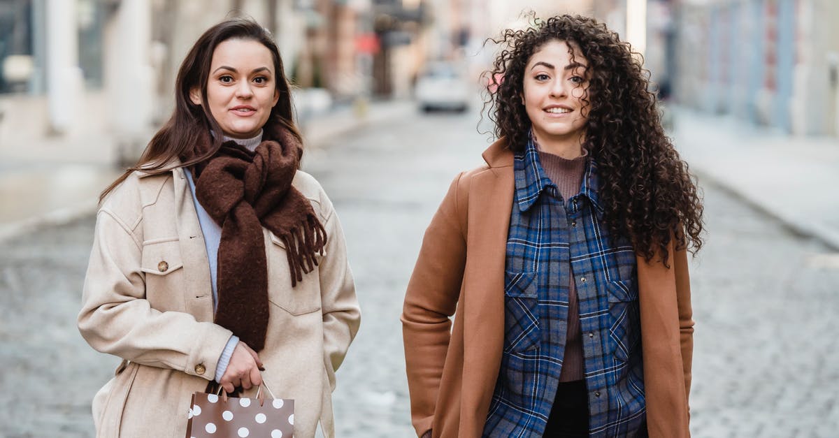 Should a student carry a sleeping bag with himself when going abroad? [closed] - Smiling multiracial girlfriends with hands in pockets standing on paved street with gift bags and looking at camera