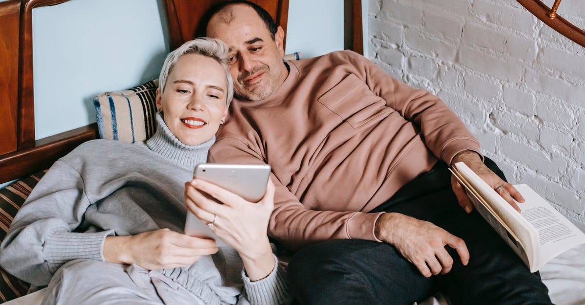 Should I book my apartment now or while I'm there? [closed] - From above of happy adult diverse couple in casual outfits lying on bed and sharing table during weekend at home