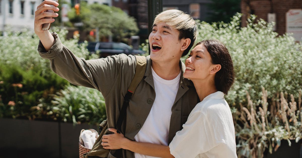 Should I insist on a refund or take Ryanair's offer to move travel date free of charge? [closed] - Cheerful young Asian couple in stylish clothes cuddling and smiling while taking selfie on mobile phone during date in city