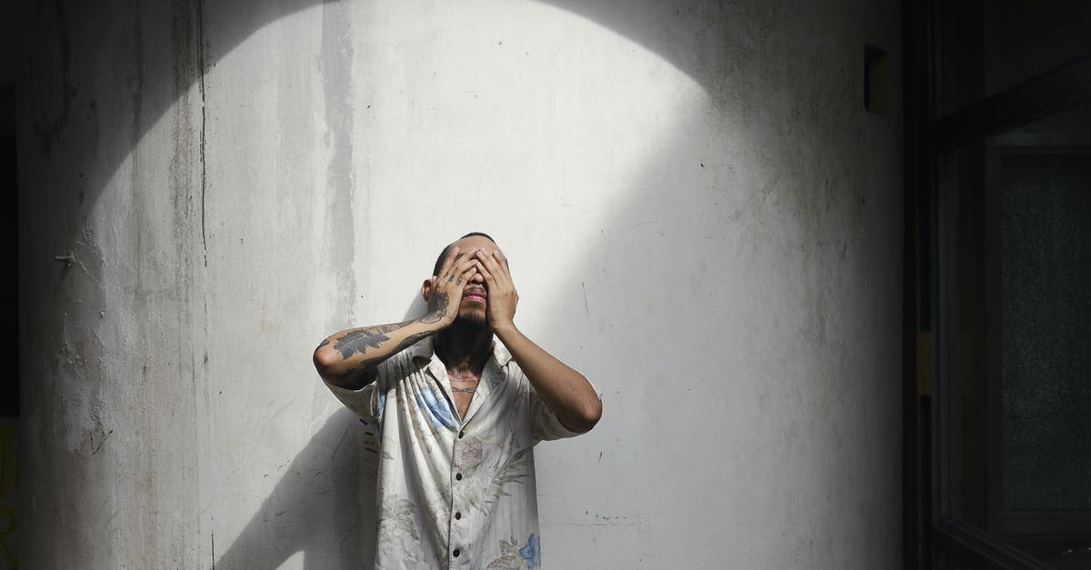 Should I just cover my forearm tattoo in Japan - Young man with short brown hair and tattoos on arm in shirt standing near white wall and closing eyes with hands Should I just cover my forearm tattoo in Japan - Young man with short brown hair and tattoos on arm in shirt standing near white wall and closing eyes with hands