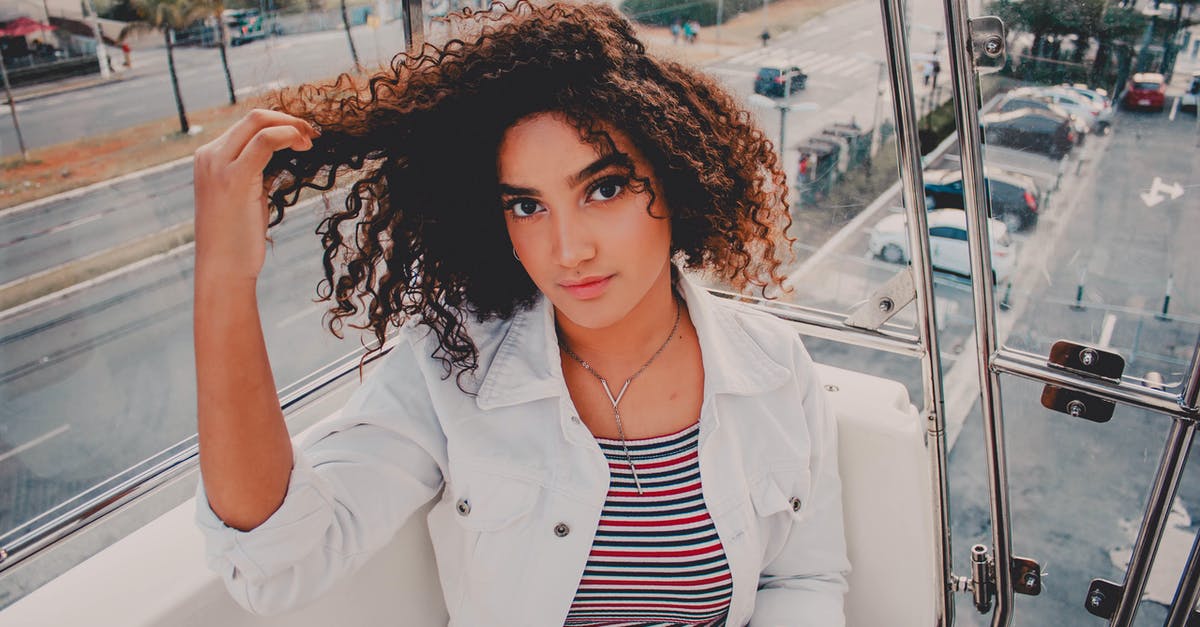 Should I wear a jacket on my trip to the Philippines? [closed] - Young ethnic woman in jacket and striped wear touching curly hair while looking at camera in ropeway cabin in city
