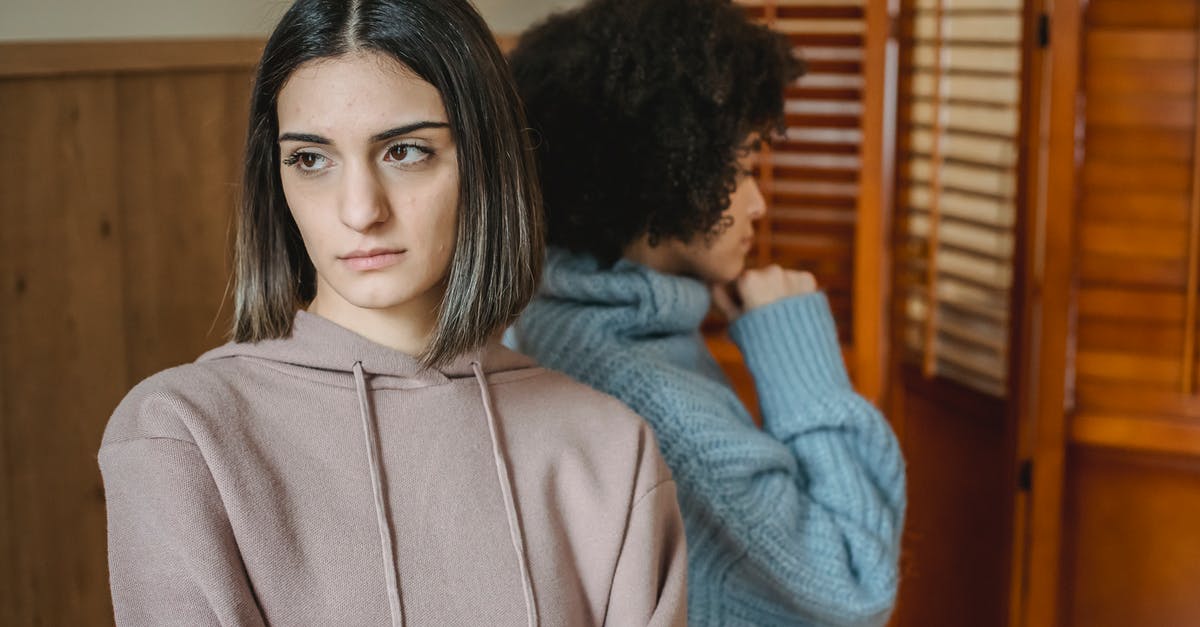 Should my friend with a drug offense as a minor apply for US visa waiver? - Upset multiracial women in casual wear standing in light room near wall with wooden folding screen while having conflict at home