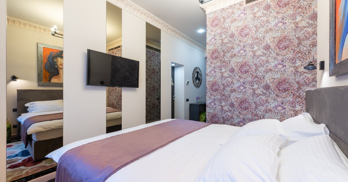 Shouldn't my insurance cover my trip interruption? [closed] - Stylish cozy light hotel suite with bed against TV hanging on wall with mirrors and wall with pink floral ornament