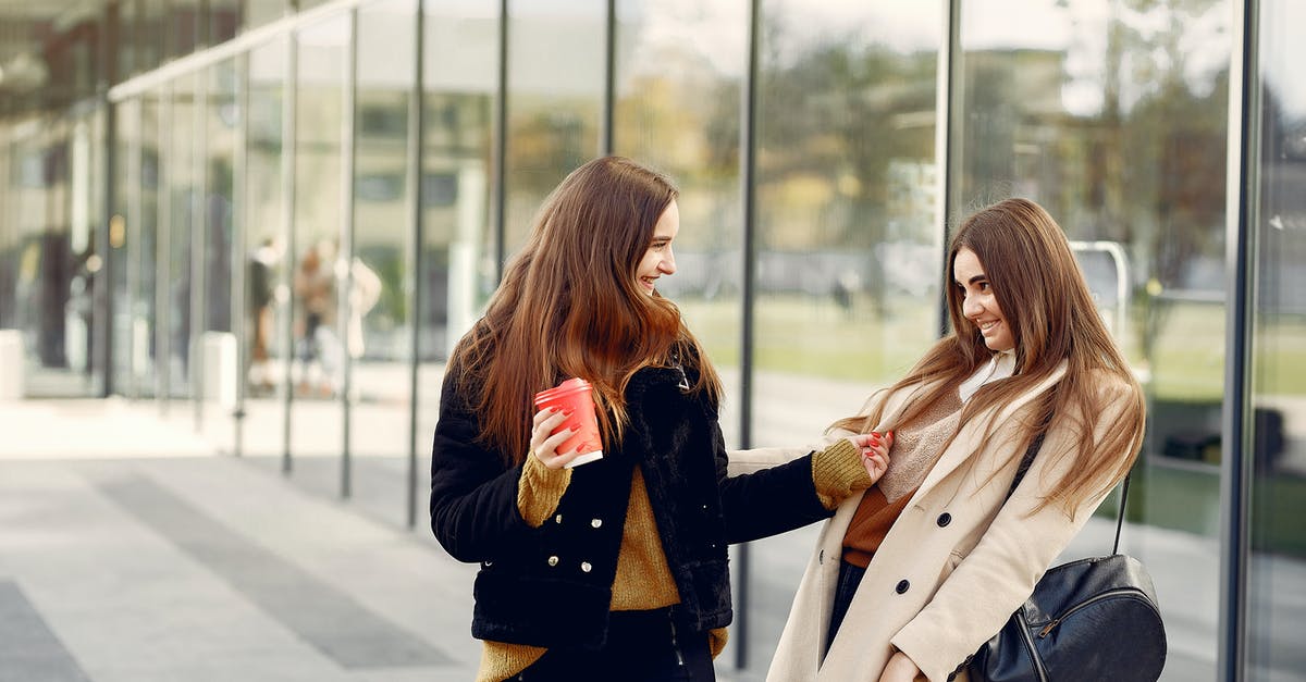 Sister seeing off student exchange - Young smiling best girlfriends in casual wear looking at each other and having fun while standing near glass building in city street Sister seeing off student exchange - Young smiling best girlfriends in casual wear looking at each other and having fun while standing near glass building in city street