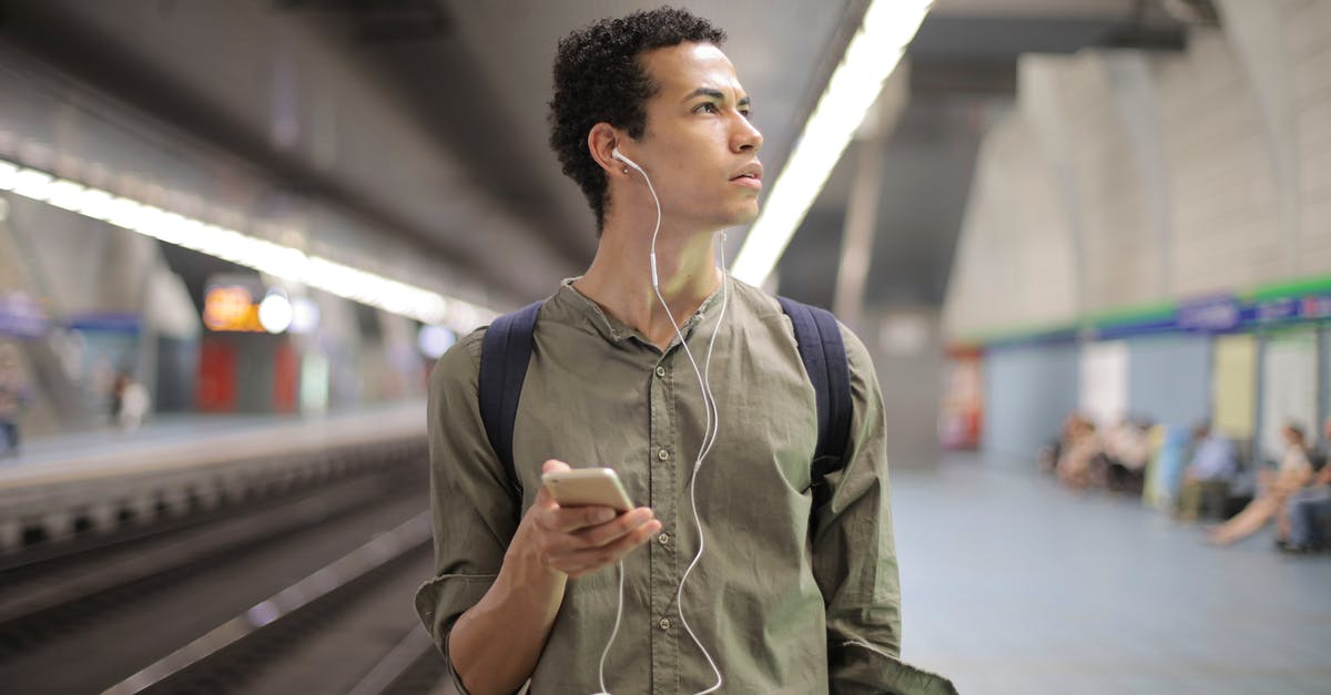 Skip train journey [duplicate] - Young ethnic man in earbuds listening to music while waiting for transport at contemporary subway station