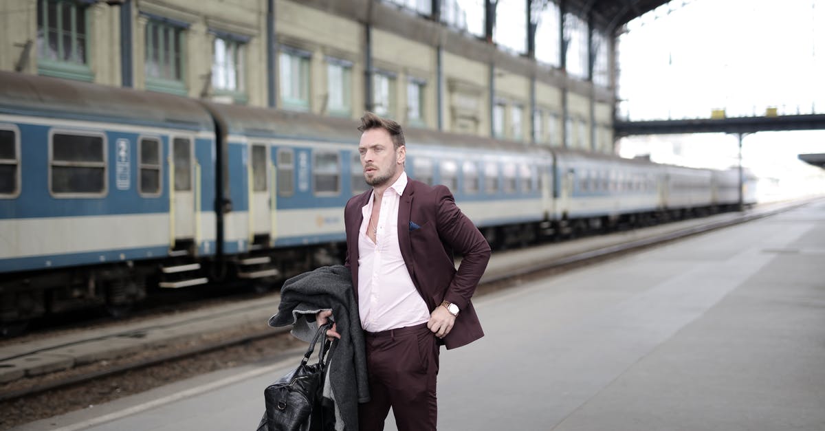 Skip train journey [duplicate] - Serious stylish businessman in elegant white shirt and purple jacket holding leather bag and coat in hand standing on platform on railway station and waiting for train