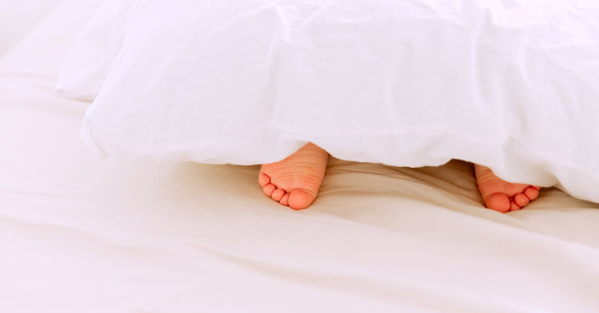 Small layover time. What to do? - Crop tiny feet of little child lying under white blanket on comfortable bed in light bedroom at home Small layover time. What to do? - Crop tiny feet of little child lying under white blanket on comfortable bed in light bedroom at home