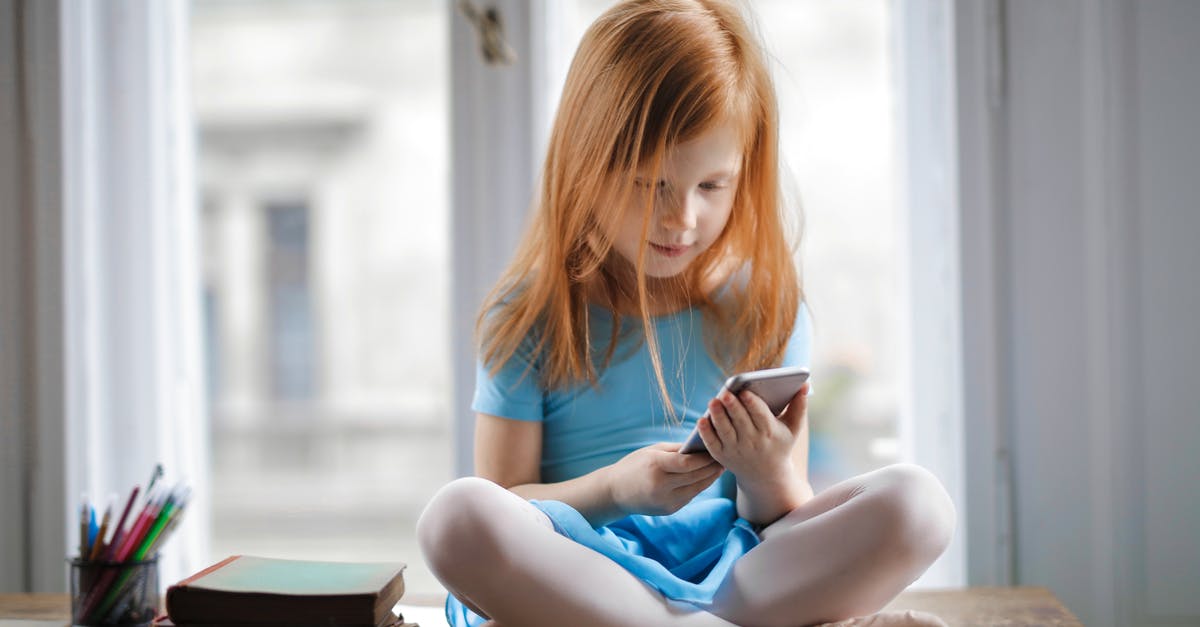 Small Mexican hotel would not take credit card to book room - Red haired charming schoolgirl in blue dress browsing smartphone while sitting on rustic wooden table with legs crossed beside books against big window at home Small Mexican hotel would not take credit card to book room - Red haired charming schoolgirl in blue dress browsing smartphone while sitting on rustic wooden table with legs crossed beside books against big window at home