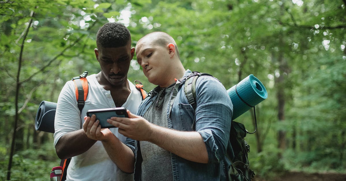 Social Travel App for managing Itinerary - Focused multi ethnic backpackers watching smartphone while finding location in woodland in daytime on blurred background Social Travel App for managing Itinerary - Focused multi ethnic backpackers watching smartphone while finding location in woodland in daytime on blurred background