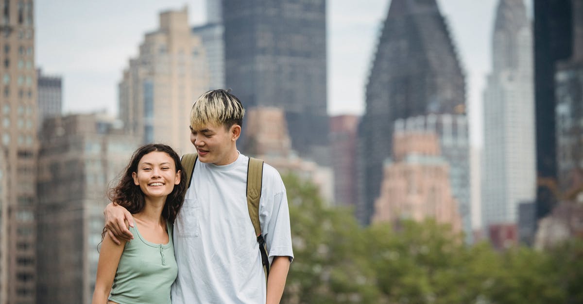 Start date for entering the US on a J-1 visa - Cheerful young Asian couple in casual clothes hugging each other and standing against modern skyscrapers while spending holidays in New York Start date for entering the US on a J-1 visa - Cheerful young Asian couple in casual clothes hugging each other and standing against modern skyscrapers while spending holidays in New York