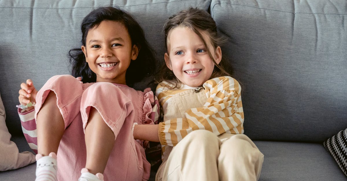 Stopover in Heathrow, do I have to secure any kind of UK visa [duplicate] - Cheerful best multiracial friends in striped clothes interacting on couch in living room in house