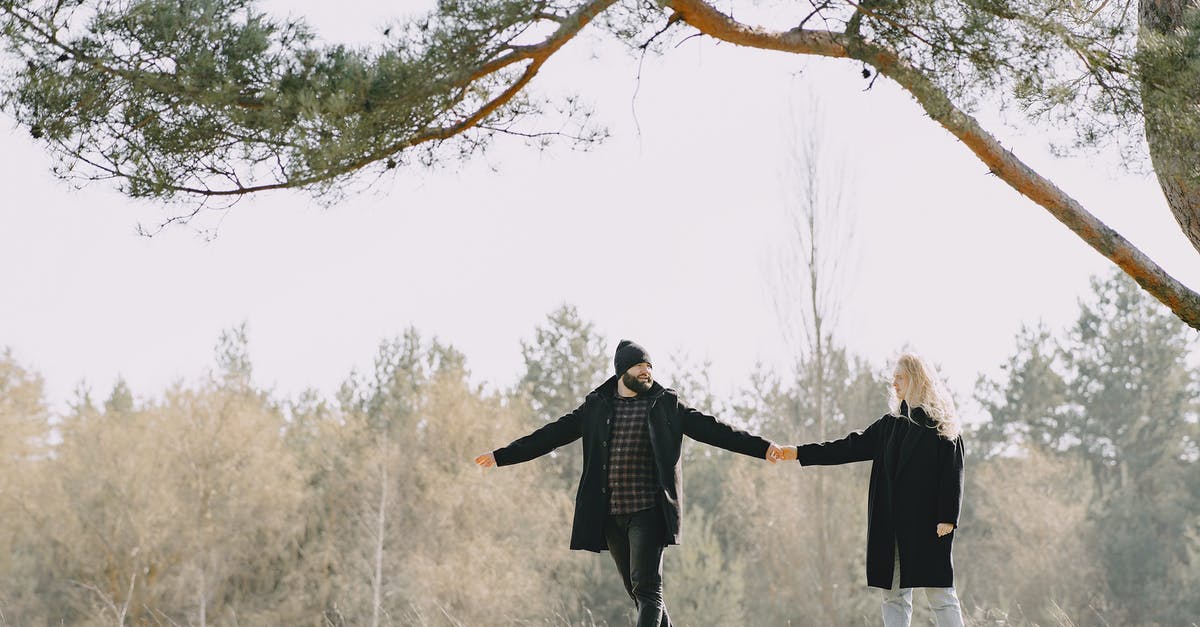 Supplies and support on a long-distance walk - Full body happy lovers in warm casual coats holding hands while spending time together in autumn park looking at each other Supplies and support on a long-distance walk - Full body happy lovers in warm casual coats holding hands while spending time together in autumn park looking at each other