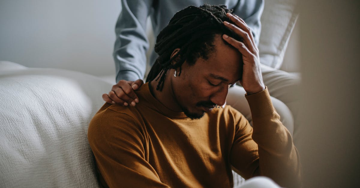 Supporting my wife for Schengen Visa application - Worried depressed African American male touching head nervously and sitting with eyes closed near supporting wife in bedroom Supporting my wife for Schengen Visa application - Worried depressed African American male touching head nervously and sitting with eyes closed near supporting wife in bedroom