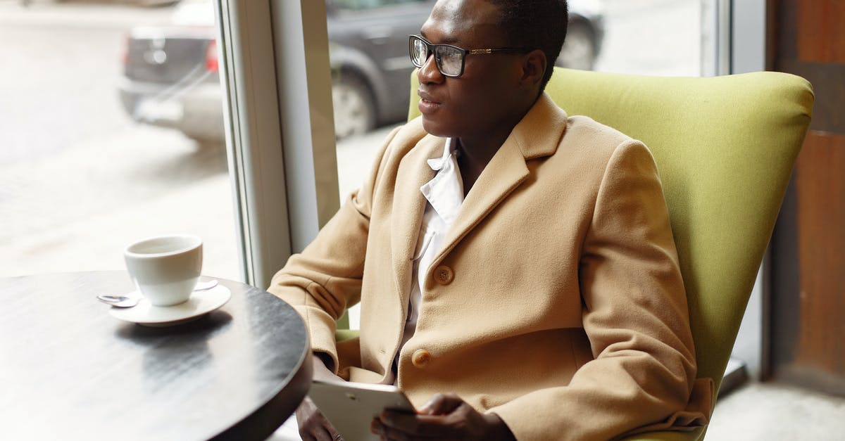 Surfing in Sri Lanka in August - Serious African American male in trendy formal suit and eyeglasses sitting on cozy chair in cafe with cup of coffee and browsing tablet Surfing in Sri Lanka in August - Serious African American male in trendy formal suit and eyeglasses sitting on cozy chair in cafe with cup of coffee and browsing tablet