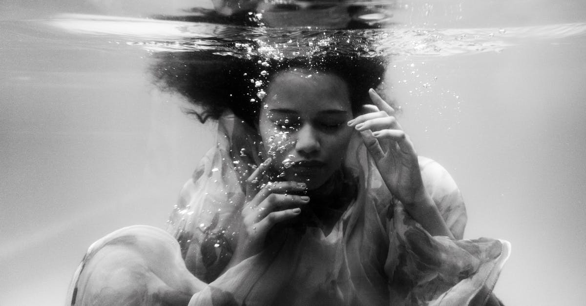 Swimming pool dressing code in Luxembourg - Black and white unemotional young female in loose dress diving with eyes closed into seawater