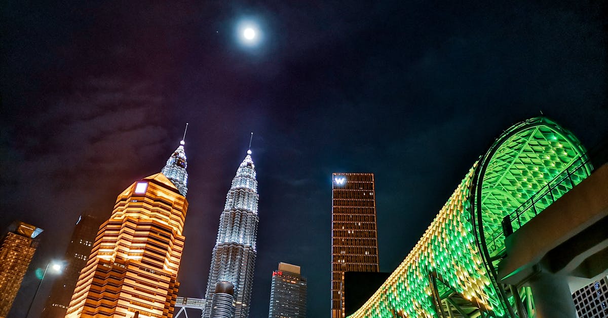 Time to get to KUL from center of Kuala Lumpur - From below exterior of contemporary Petronas Twin Towers located amidst urban city towers and pedestrian overpass illuminated by electrical lights at night Time to get to KUL from center of Kuala Lumpur - From below exterior of contemporary Petronas Twin Towers located amidst urban city towers and pedestrian overpass illuminated by electrical lights at night