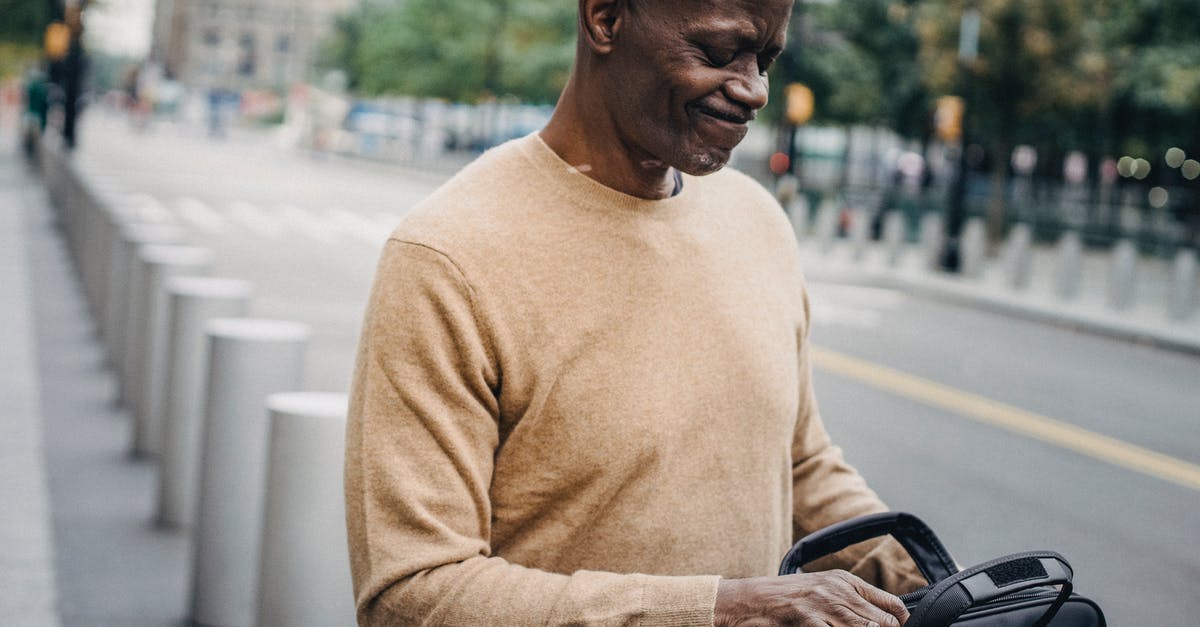 Tips to avoid forgetting a bag - Frowning black businessman with personal case looking inside and grimacing while standing in street Tips to avoid forgetting a bag - Frowning black businessman with personal case looking inside and grimacing while standing in street