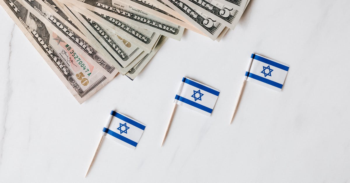 Toll charges issued in a different country - Top view of bundle of different nominal pars dollars and Israeli flags on toothpicks placed on white surface of marble table Toll charges issued in a different country - Top view of bundle of different nominal pars dollars and Israeli flags on toothpicks placed on white surface of marble table