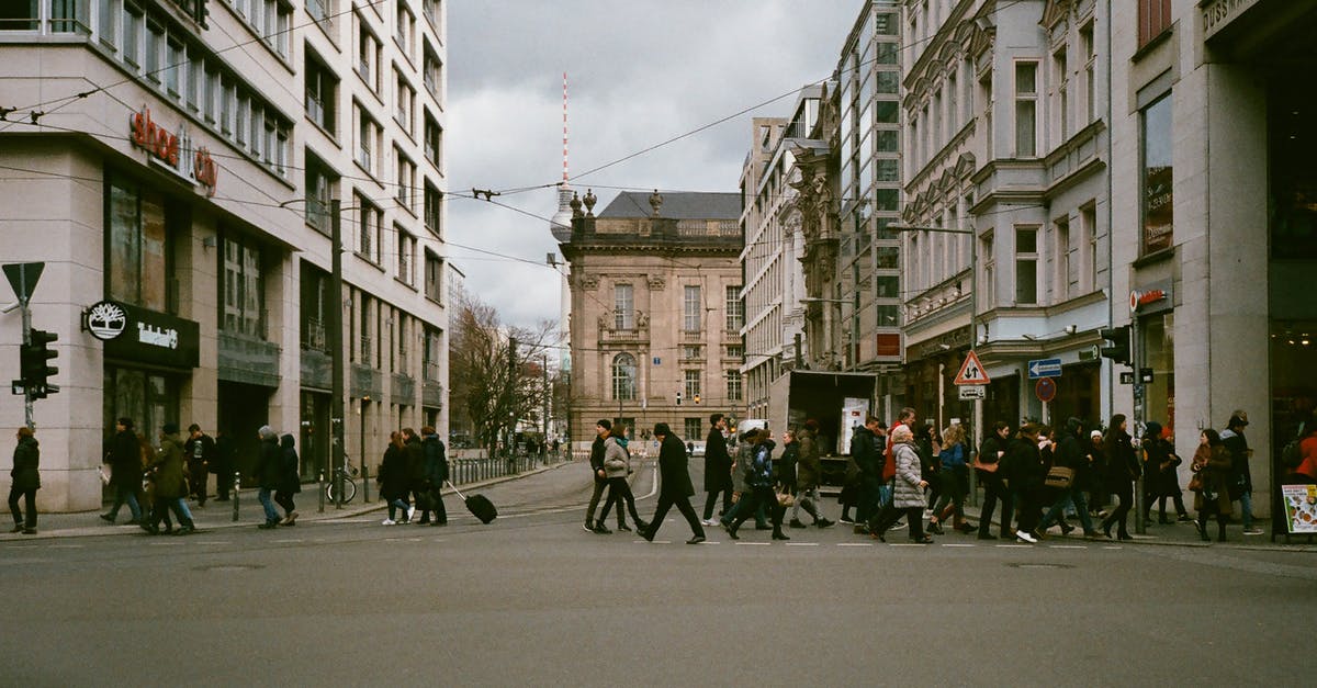 Tourism in the Schengen area either side of a student visa - Side view of unrecognizable pedestrians crossing road near old residential buildings in city on overcast day Tourism in the Schengen area either side of a student visa - Side view of unrecognizable pedestrians crossing road near old residential buildings in city on overcast day
