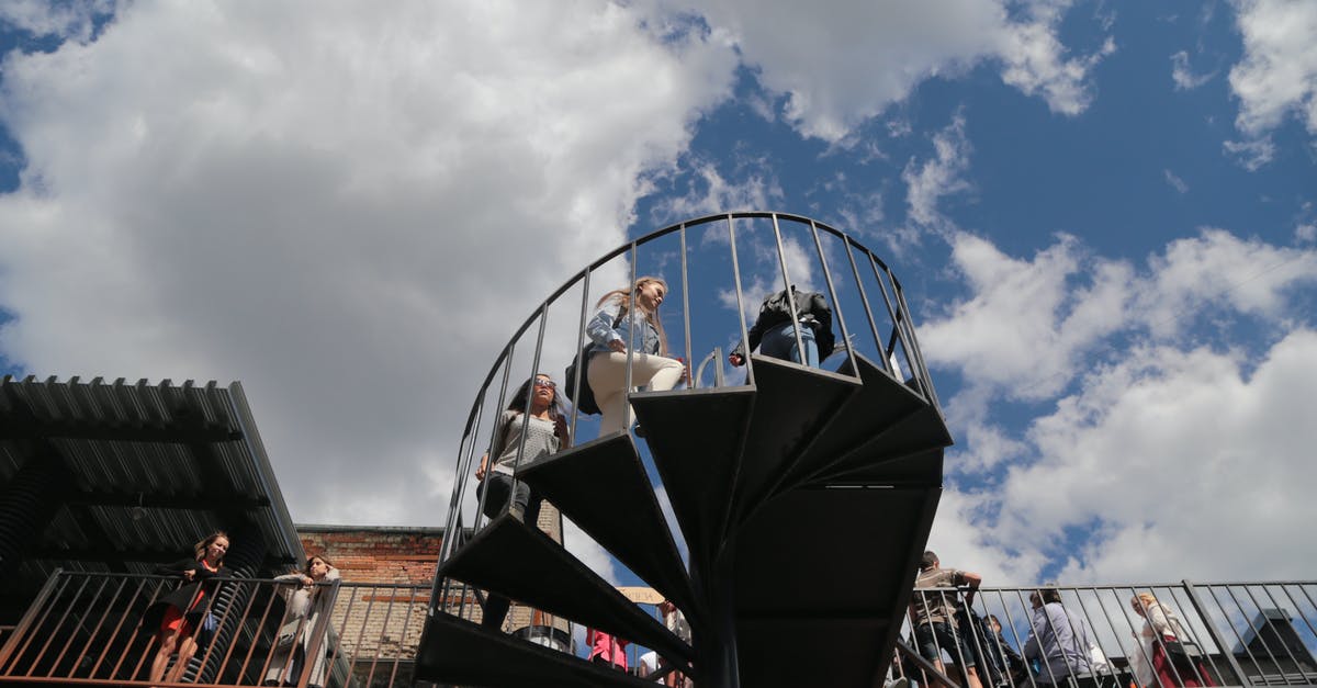 Tourist / simple city maps to print - From below of people on spiral stairway and building terrace with railing under cloudy blue sky in daytime Tourist / simple city maps to print - From below of people on spiral stairway and building terrace with railing under cloudy blue sky in daytime