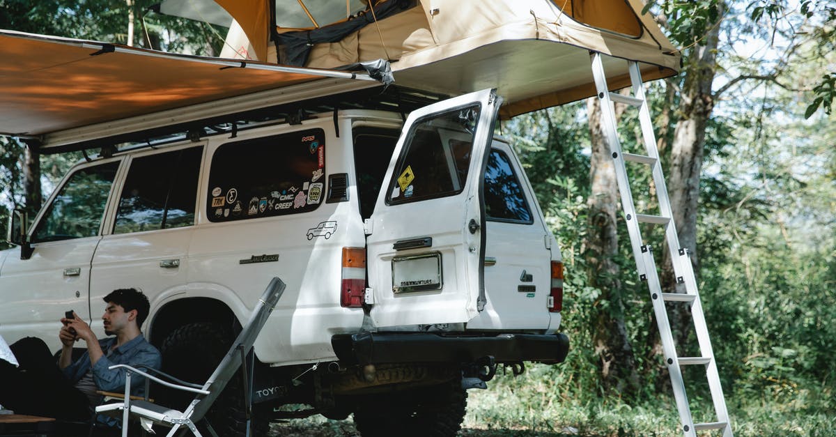 Tourist cell phone use in Myanmar - Man sitting under awning placed near offroader with tent on roof in forest Tourist cell phone use in Myanmar - Man sitting under awning placed near offroader with tent on roof in forest