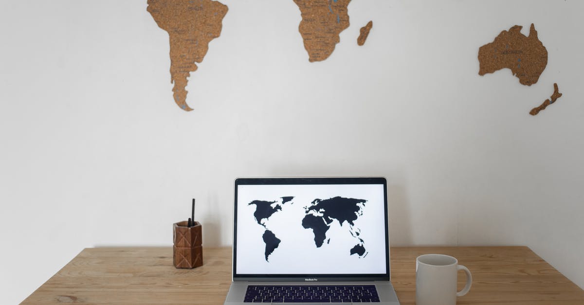 Train travel in Russia between host cities during Football World Cup 2018 - Black world map on laptop screen and ceramic cup with pen container placed on table against silhouettes of continents Train travel in Russia between host cities during Football World Cup 2018 - Black world map on laptop screen and ceramic cup with pen container placed on table against silhouettes of continents