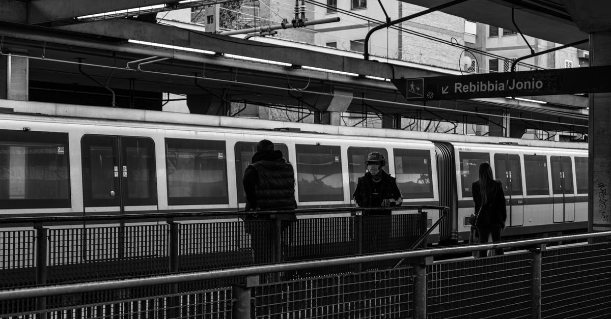 Transfer to train in Munich - Black and white of citizens on railway station walking on platform near public train against modern buildings in city center Transfer to train in Munich - Black and white of citizens on railway station walking on platform near public train against modern buildings in city center