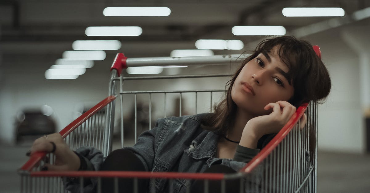Transit accessible parking lots near Amsterdam - Dreamy female with black hair and head tilted to side with hand near face sitting in metal cart while looking at camera on blurred underground parking lot Transit accessible parking lots near Amsterdam - Dreamy female with black hair and head tilted to side with hand near face sitting in metal cart while looking at camera on blurred underground parking lot