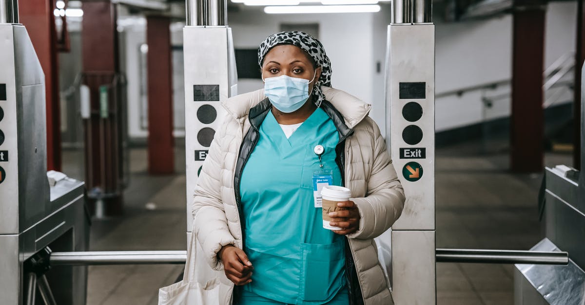 Transport pass for one week in Mallorca - Calm adult African American nurse with coffee to go wearing warm outfit and protective face mask passing through turnstile in metro station and looking at camera Transport pass for one week in Mallorca - Calm adult African American nurse with coffee to go wearing warm outfit and protective face mask passing through turnstile in metro station and looking at camera