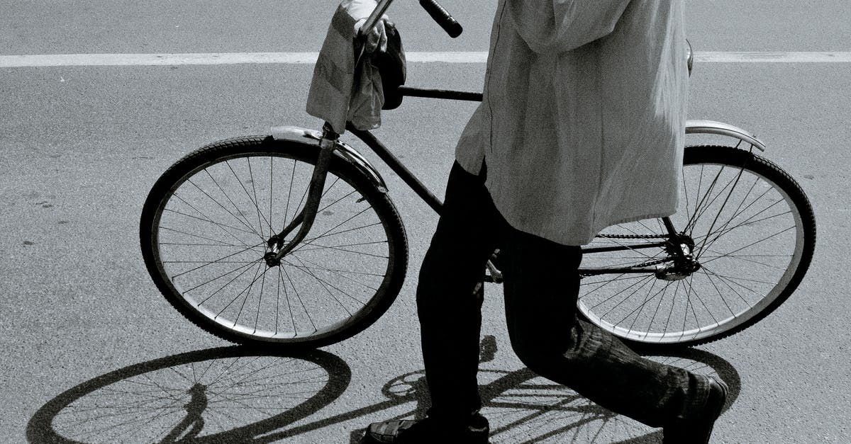 Transporting (not riding) a tandem bicycle from Tangier to Essaouira - Side view of black and white crop anonymous person in stylish outfit walking on asphalt road with bicycle on sunny day Transporting (not riding) a tandem bicycle from Tangier to Essaouira - Side view of black and white crop anonymous person in stylish outfit walking on asphalt road with bicycle on sunny day