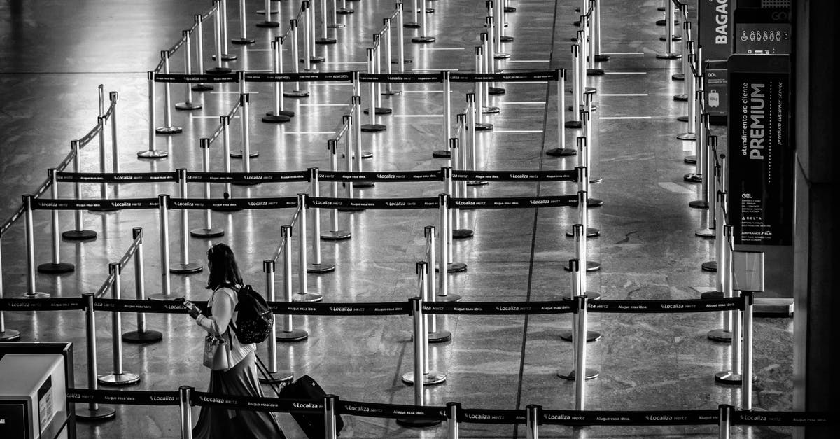 Travel from Lyon to Geneva Airport (French side) - From above black and white side view of unrecognizable female tourist with backpack and suitcase strolling on fenced passage in airport Travel from Lyon to Geneva Airport (French side) - From above black and white side view of unrecognizable female tourist with backpack and suitcase strolling on fenced passage in airport