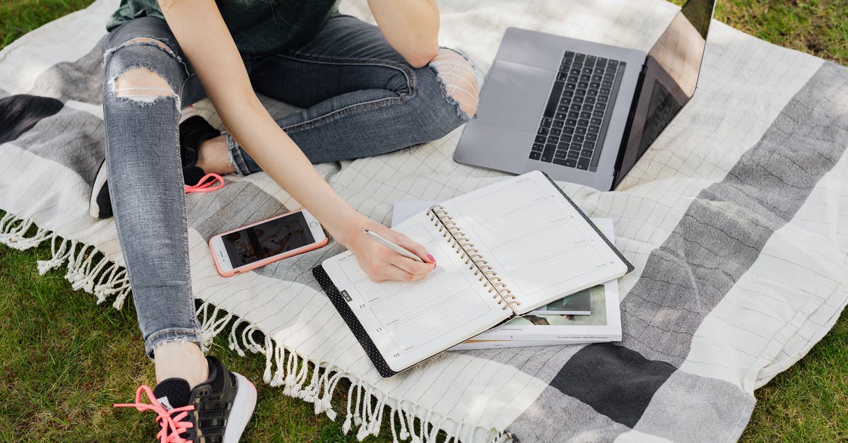 Travel planner app/website to plan by attractions/beaches/zoo/amusement park/pubs/Uber - From above crop anonymous female student in casual outfit writing in planner while sitting on warm blanket with smartphone and laptop on green park lawn Travel planner app/website to plan by attractions/beaches/zoo/amusement park/pubs/Uber - From above crop anonymous female student in casual outfit writing in planner while sitting on warm blanket with smartphone and laptop on green park lawn