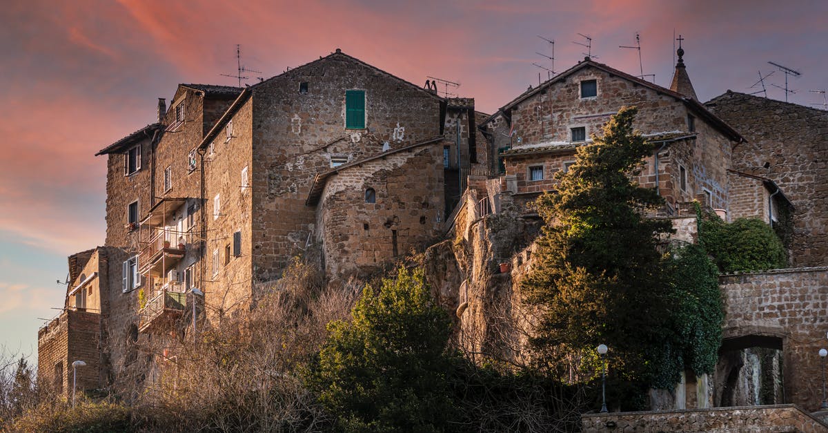 Travel to Italy from the UK - From below of aged stone houses of Calcata medieval town located on hill top under amazing sundown sky Travel to Italy from the UK - From below of aged stone houses of Calcata medieval town located on hill top under amazing sundown sky