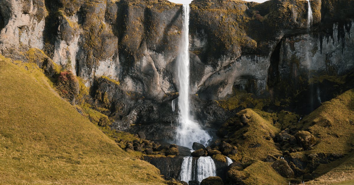 Traveling around Schengen Area with a single entry Iceland Visa - Picturesque distance scenery of small waterfall falling off tuffstone cliffs and green slopes with cattle grazing at foot of mountains during daytime Traveling around Schengen Area with a single entry Iceland Visa - Picturesque distance scenery of small waterfall falling off tuffstone cliffs and green slopes with cattle grazing at foot of mountains during daytime