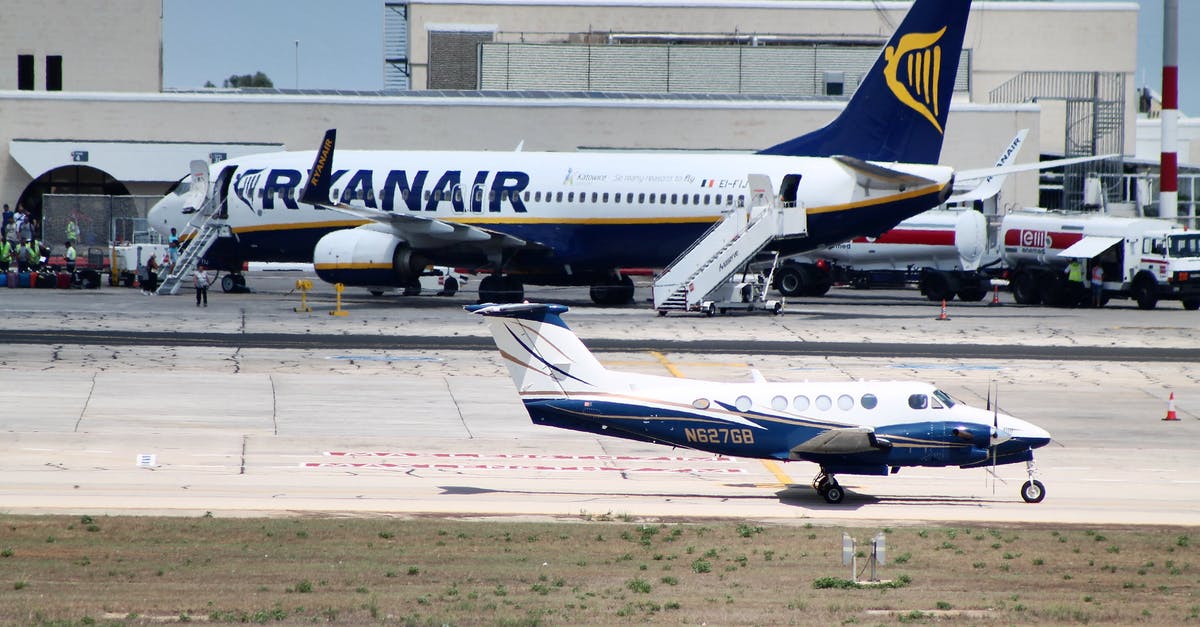 Traveling internationally with one-way airline tickets - Civil utility and narrow body aircraft parked on runway tracks near modern airport building against cloudless blue sky