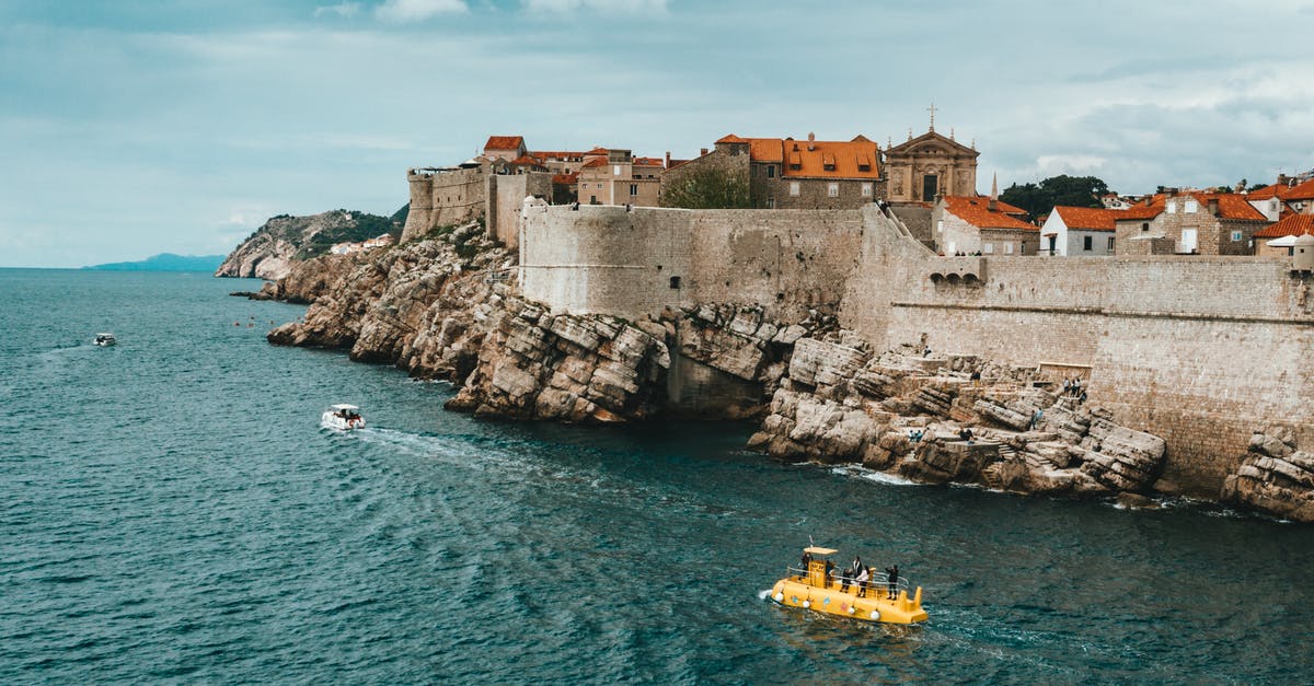 Traveling on cruise ship from Italy to Croatia - Modern boats floating on rippling sea near rocky coast of old town of Dubrovnik with historical buildings and ancient city walls Traveling on cruise ship from Italy to Croatia - Modern boats floating on rippling sea near rocky coast of old town of Dubrovnik with historical buildings and ancient city walls