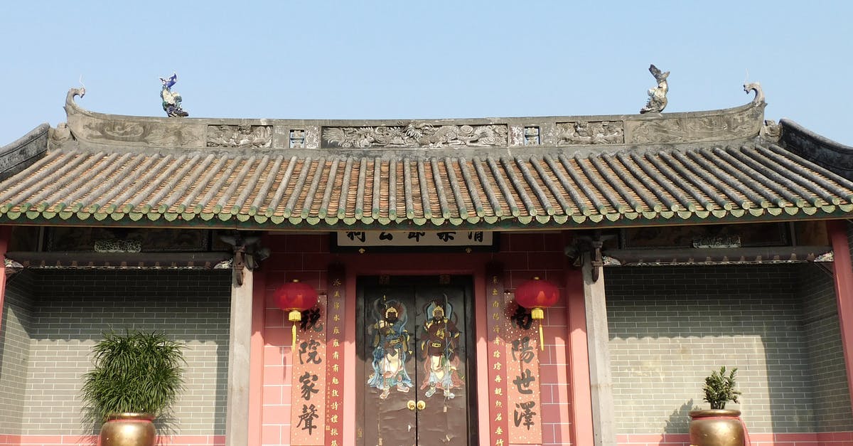Traveling to China transfer in Hong Kong. Do I need a HK transit visa? [duplicate] - Exterior of ancient Buddhist Tang Ching Lok ancestral hall with hieroglyphs near ornamental doors and potted plant against cloudless blue sky in Hong Kong