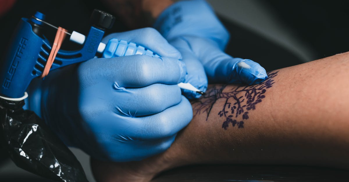 Traveling to Korea with special entry procedure because of COVID-19 - From above of faceless tattooist in blue gloves applying tree tattoo with ink and professional machine on leg of anonymous client in salon Traveling to Korea with special entry procedure because of COVID-19 - From above of faceless tattooist in blue gloves applying tree tattoo with ink and professional machine on leg of anonymous client in salon